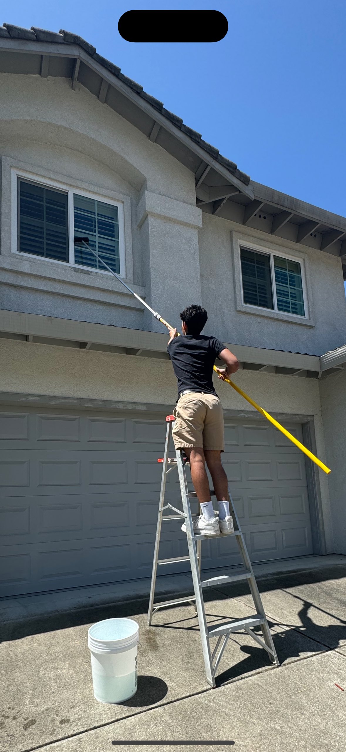 Professional window cleaner on ladder cleaning house exterior windows with professional equipment